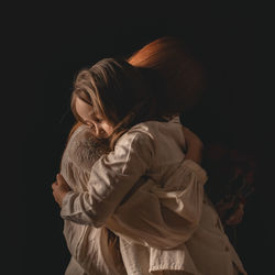 Mother and daughter hugging against black background