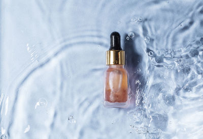 Mockup of cosmetic glass pink bottle with pipette and serum on water surface