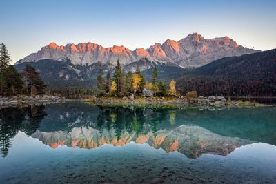 Scenic view of lake by mountains against clear sky during sunset