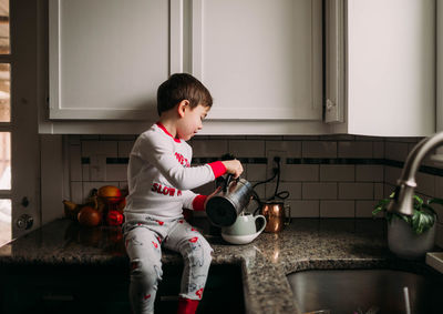 Young boy sitting on kitchen counter pouring milk into coffee