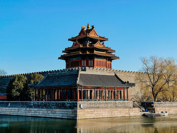 Traditional building by lake against clear blue sky