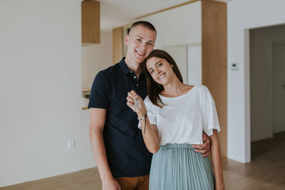 Portrait of smiling young couple with house key standing at home