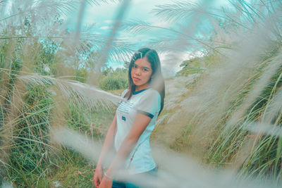 Portrait of young woman standing by plants on land