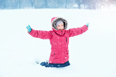 Cheerful girl with arms outstretched kneeling on snow covered land