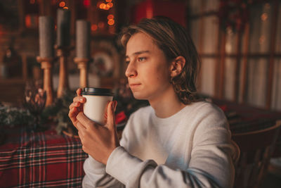 Portrait of candid authentic smiling handsome boy teenager using mobile phone at xmas home interior