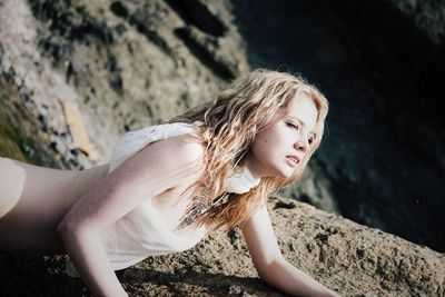 Beautiful young woman leaning on rock at shore