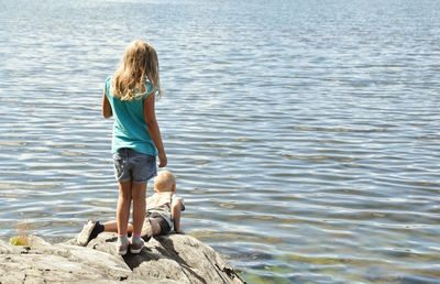 Rear view of boys standing on rock by sea