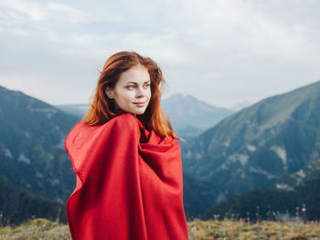 Portrait of beautiful young woman standing against mountains