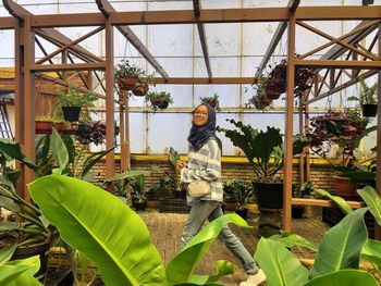 Woman standing by potted plants in greenhouse