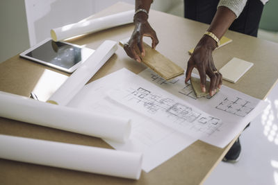 Mature female architect preparing designs modules over blueprint while working at under construction apartment