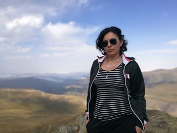 Woman wearing sunglasses standing on mountain against sky