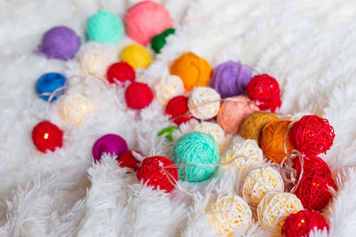 A lot of colorful knitting yarn and a luminous garland in the form of balls lie on fluffy blanket.