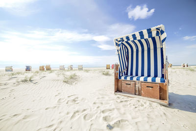 Hooded chairs on beach against sky