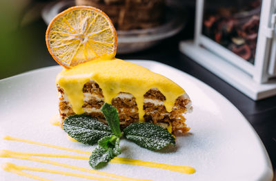 Piece of carrot cake with yellow glaze, dried orange and garnished with mint