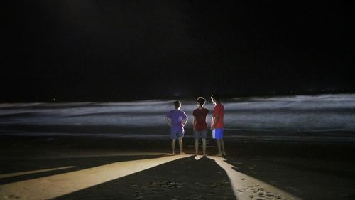 People standing on beach against sky at night