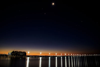 Illuminated city by river against sky at night