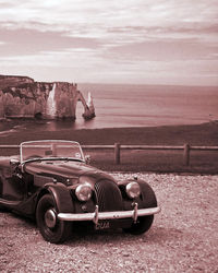 Vintage car on land by sea against sky