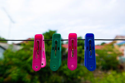 Close-up of clothespins hanging on clothesline against sky