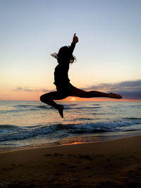 Silhouette man jumping at beach against sky during sunset