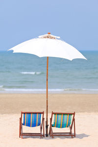 Deck chairs on beach against sky