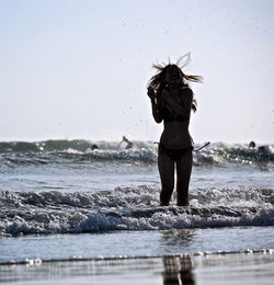 Rear view of woman standing on beach against clear sky