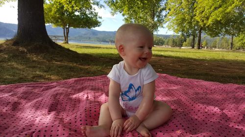 Cute baby girl sitting on blanket by tree 