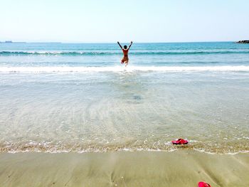 Man jumping on beach against clear sky