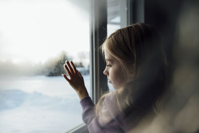 Thoughtful girl standing by window at home