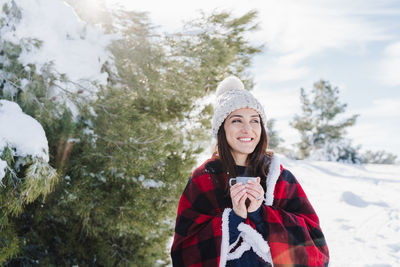 Smiling woman standing with coffee cup in snow