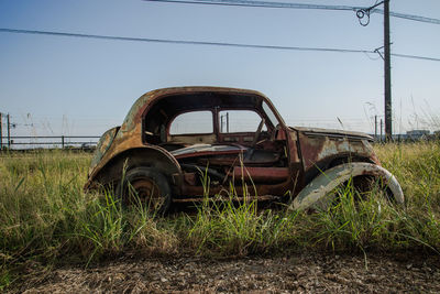 Abandoned car on field against clear sky