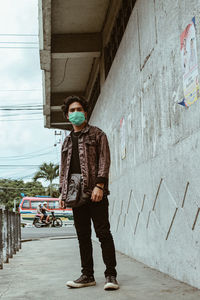 Full length of man wearing mask standing against wall outdoors