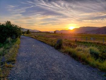 Road amidst field against sky during sunset