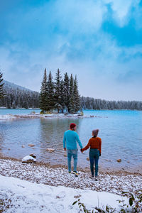 Rear view of men standing by lake against sky during winter