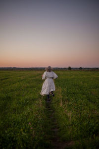 Rear view of woman standing on field against sky during sunset