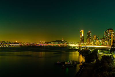 Illuminated city by river against sky at night