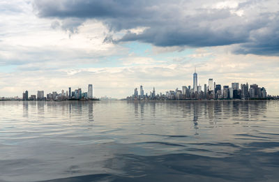 River and modern buildings in city against cloudy sky