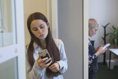 Two young women checking their smart phones in an office space.