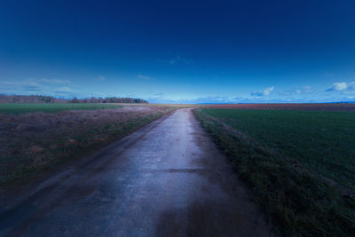 Empty road amidst field against blue sky