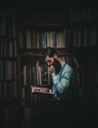 Man reading book while standing against shelves