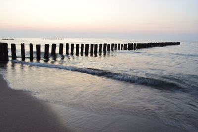 Wooden posts on beach against sky during sunset