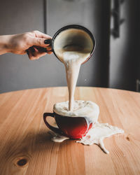 Close-up of hand pouring coffee cup on table