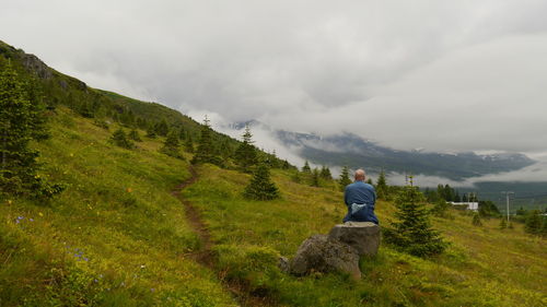 Rear view of wanderer resting on rock while viewing the foggy mountainrange