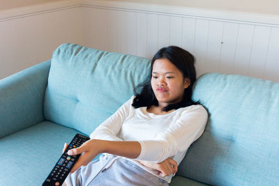 Asian teenage girl sitting on sofa watch television