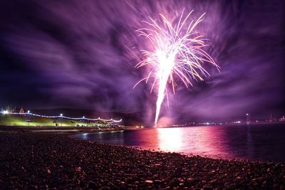 Firework display over sea against sky at night