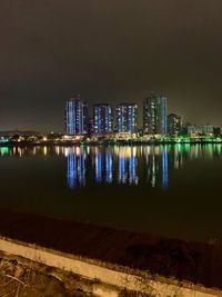 Illuminated buildings by river against sky at night
