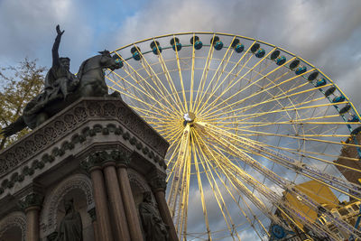 Low angle view of ferris wheel against cloudy sky