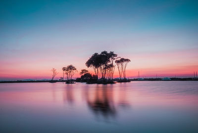 Silhouette trees by sea against romantic sky at sunset