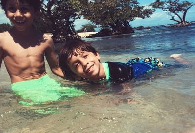 Portrait of brothers swimming in sea against sky