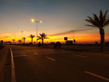 Road by illuminated city against sky during sunset