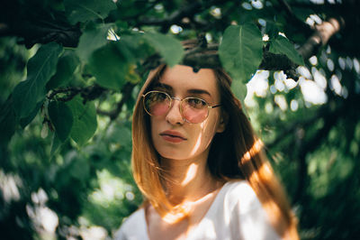 Portrait of young woman wearing sunglasses by leaves on branches